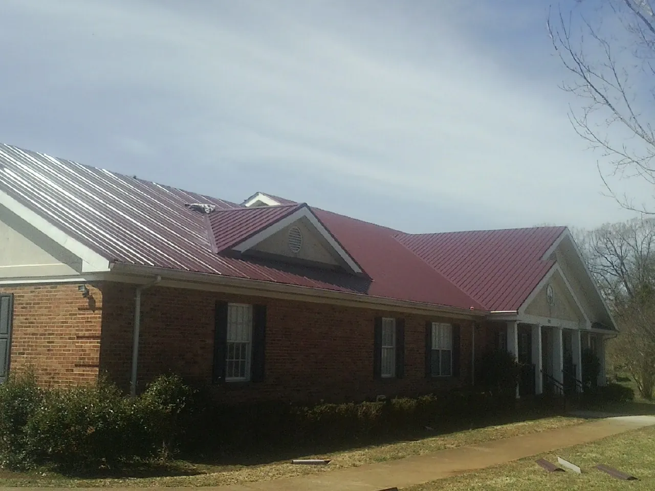 Red metal roof with gabled entries on a long brick building, from a Hail Damage Roof Repair job in Monteview