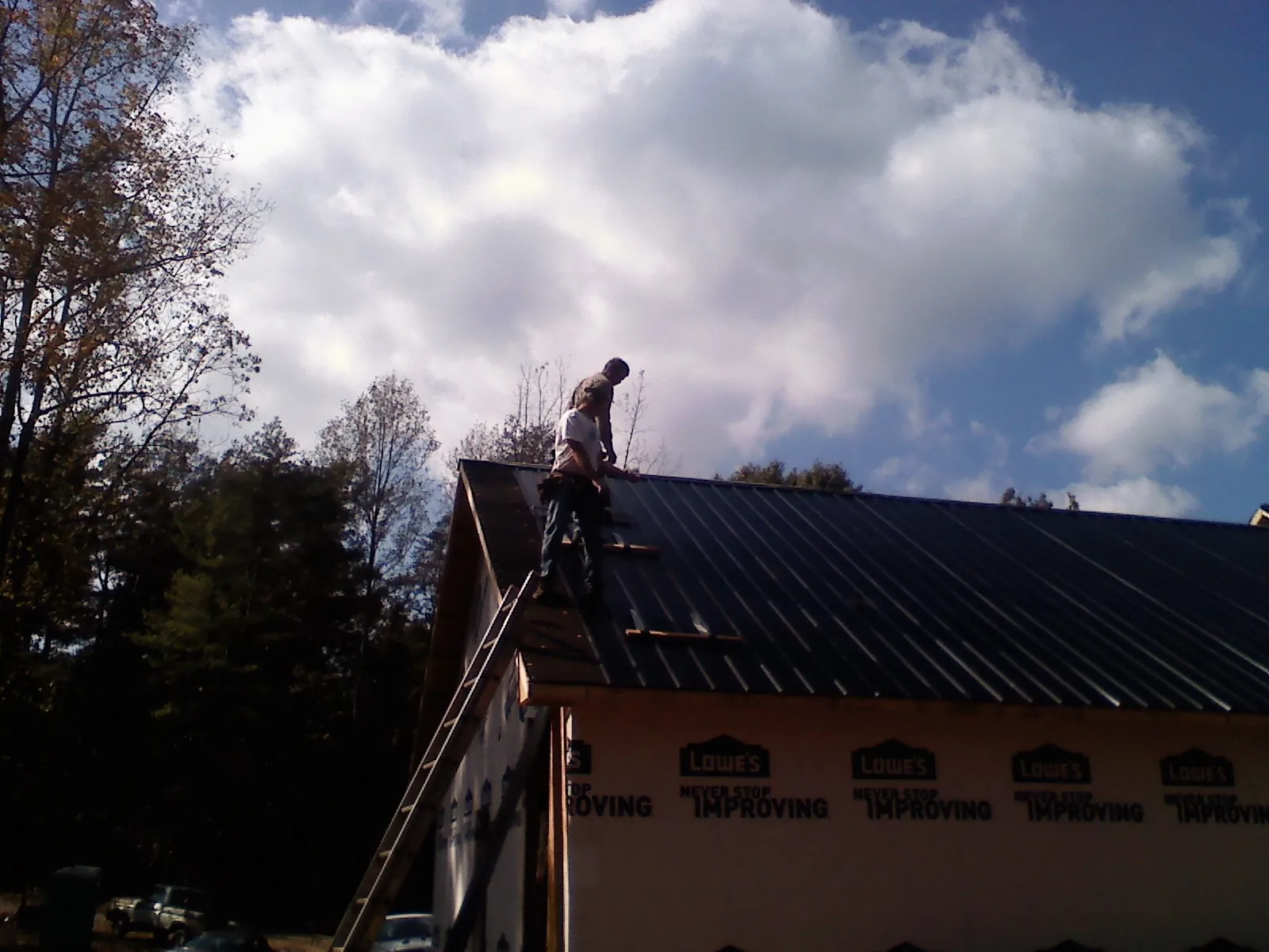 Roofer fastening dark metal panels high against a cloudy sky, from a Roof Inspection job in Monteview
