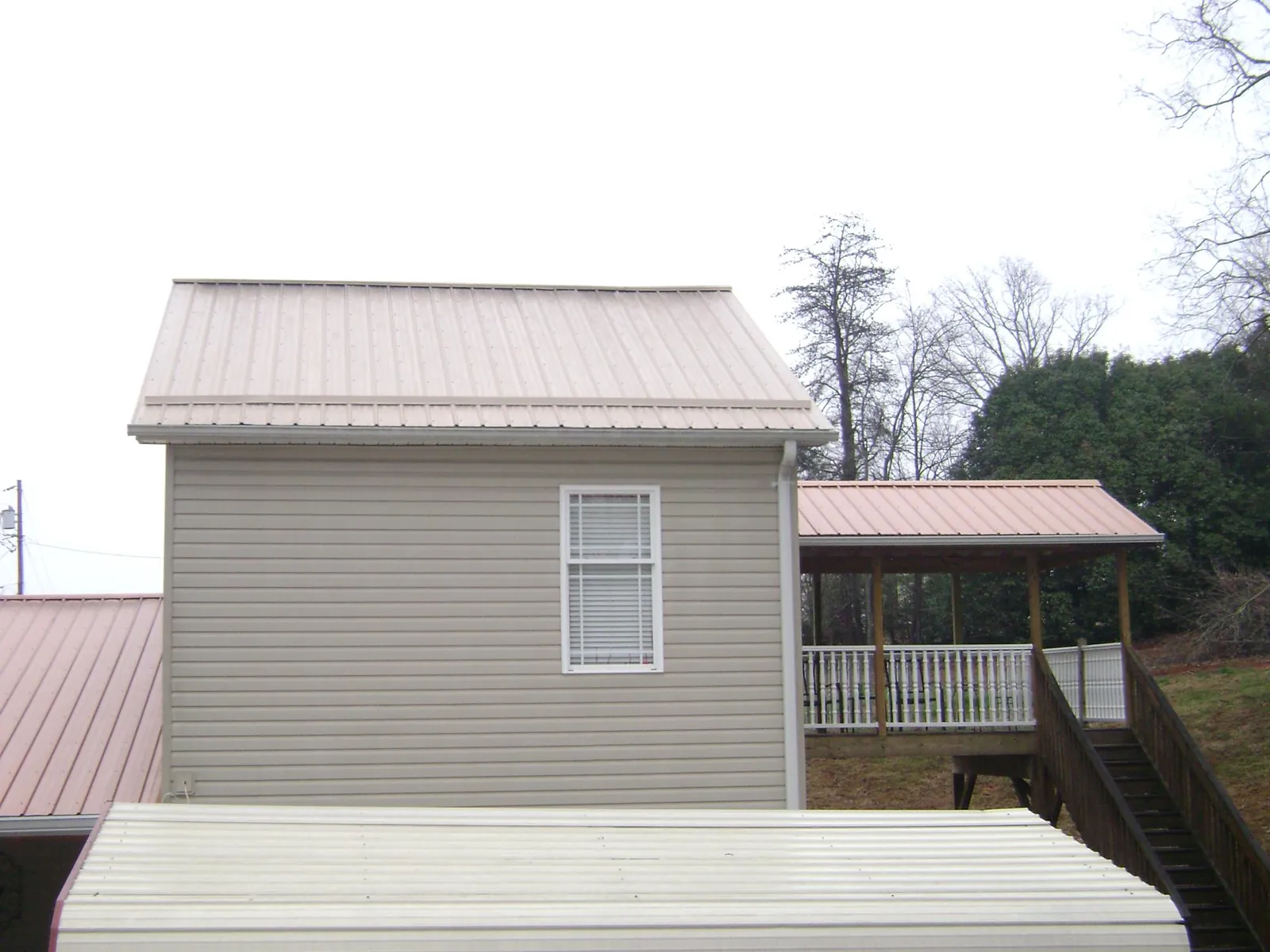 Tan metal roofs on a two story addition and attached porch, from a Roof Replacement job in Monteview